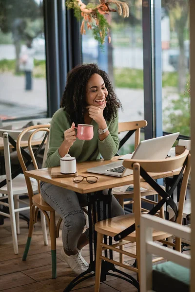 Feliz Afro Americana Segurando Xícara Café Enquanto Olha Para Laptop — Fotografia de Stock