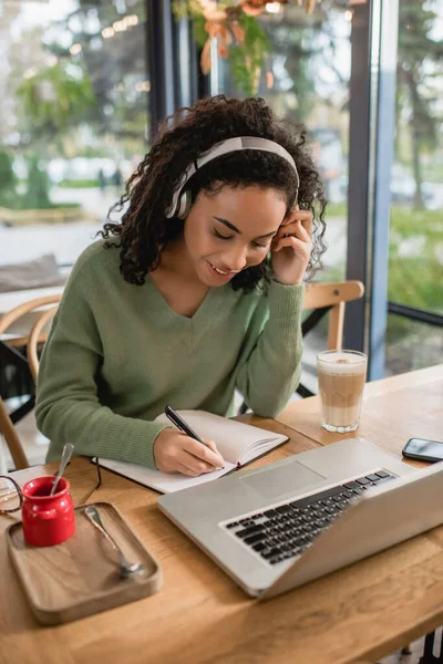 Lycklig Afrikansk Amerikansk Kvinna Lyssnar Podcast Hörlurar Och Skriva Anteckningsbok — Stockfoto