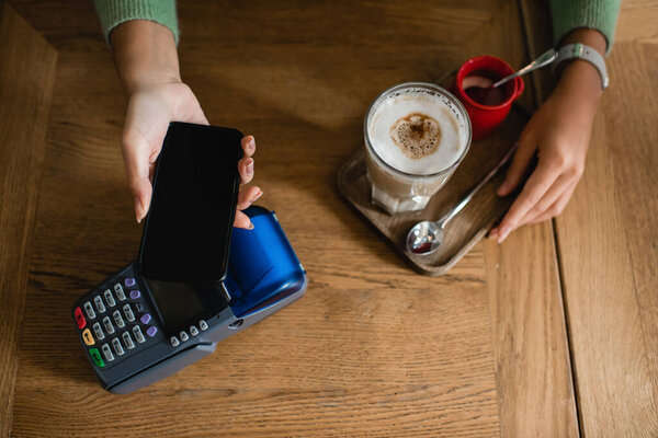 top view of african american woman paying for coffee with smartphone