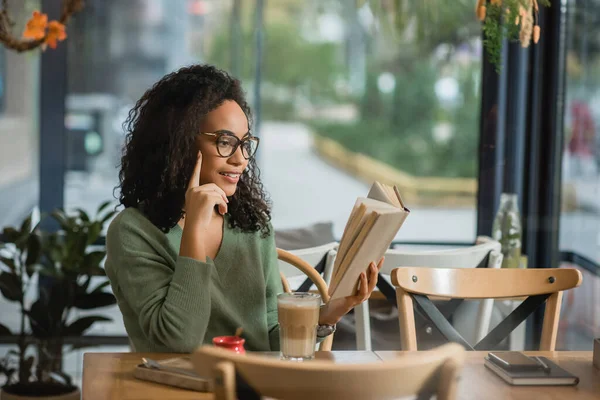 Veselá Africká Americká Žena Brýlích Čtení Knihy Skla Latté Kavárně — Stock fotografie