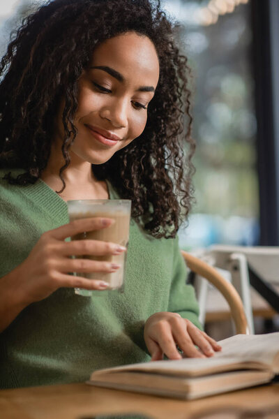 Африканская американка держит стакан с латте во время чтения книги