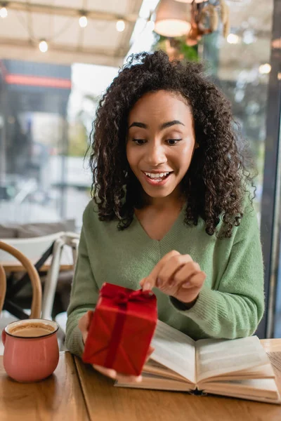 Счастливая Американка Африки Тянет Ленточку Подарочную Коробку Красным Рождеством Кафе — стоковое фото