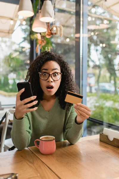 Shocked African American Woman Holding Smartphone Credit Card Cafe — Stock Photo, Image