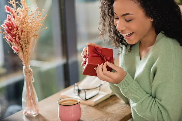 Happy African American Woman Pulling Ribbon Wrapped Christmas Present Cafe — Stock Photo, Image