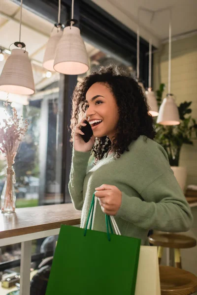 아프리카계 미국인 여성이 스마트폰으로 이야기하고 카페에서 쇼핑백을 했습니다 — 스톡 사진