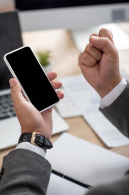 Cep telefonunu boş ekran, bulanık ön plan ile tutarken başarılı simsarın zafer jestini gösteren kısmi görünüm