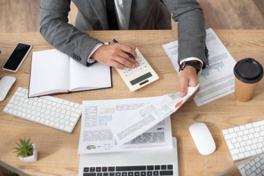 partial view of trader working with infographics and calculator near smartphone and keyboards clipart