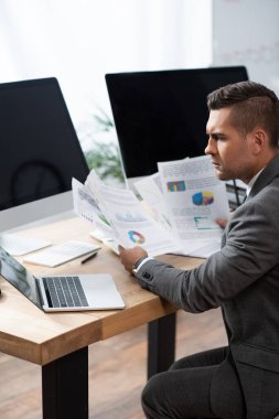 Bilgisayarın yanında bilgi ve boş ekranlı monitörler tutan düşünceli bir tüccar.
