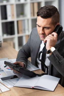İş yerinde, boş defterin yanında sabit telefondan konuşan ciddi bir işlemci.