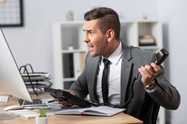 Bilgisayar ekranına bakarken şok olmuş tüccarın cep telefonu, bulanık arkaplan