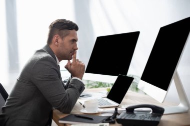 side view of trader sitting at workplace near laptop and monitors with blank screen, blurred foreground clipart