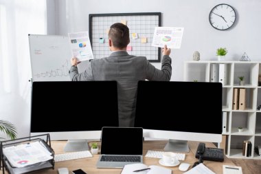 Önplanı bulanık olan boş ekranlı monitörlerin yanında bilgi taşıyan simsarın arka görünümü