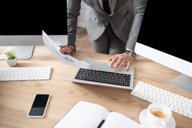 Bilgisayarın, monitörlerin ve boş ekranlı akıllı telefonun yanında bilgi taşıyan tüccarın kısmi görünümü