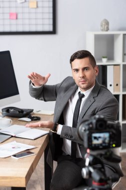trader showing amount gesture during video streaming on digital camera, blurred foreground clipart