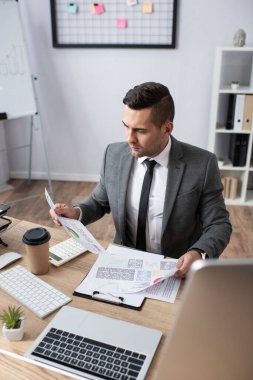 Bilgisayarın yanında bilgi grafikleriyle çalışan tüccarın yüksek açılı görünümü, bulanık önplan