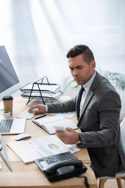 Ernstige Handelaar Typen Toetsenbord Terwijl Berichten Smartphone Het Kantoor Wazig — Stockfoto