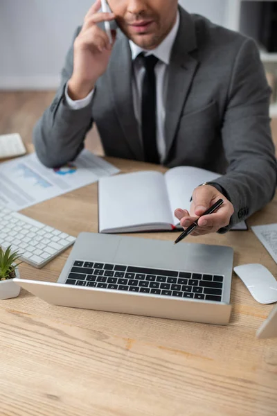 Akıllı telefondaki bulanık arkaplanda konuşurken dizüstü bilgisayarı işaret eden kırpılmış simsar görüntüsü