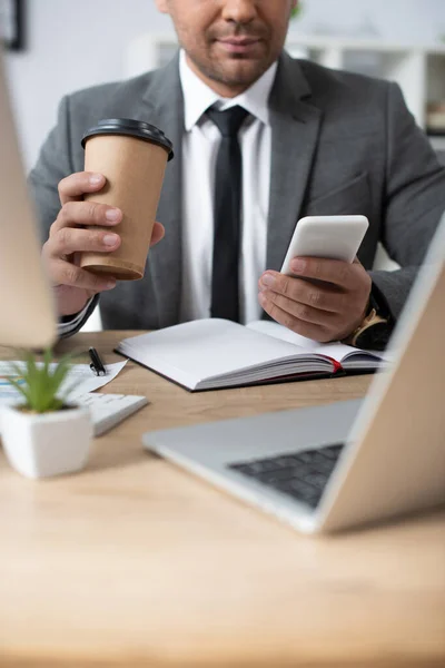 Cropped View Trader Holding Coffee While Messaging Smartphone Laptop Blurred — Stock Photo, Image