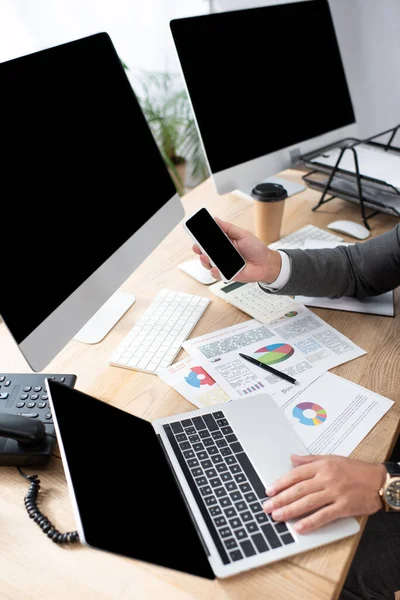 Bilgisayarın, bilgisayar monitörlerinin ve bilgi grafiklerinin yanında akıllı telefon tutan tüccarın kısmi görüntüsü