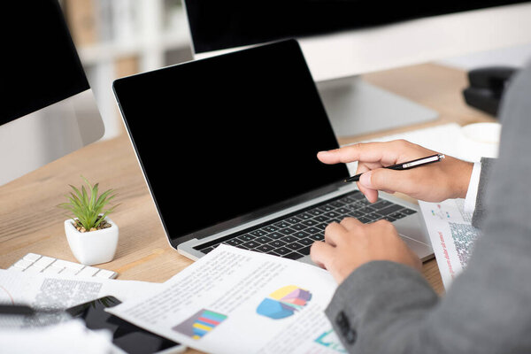 cropped view of trader pointing with finger at laptop with blank screen, blurred foreground