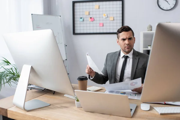 Ernstige Handelaar Holding Papieren Terwijl Zitten Werkplek Buurt Van Laptop — Stockfoto