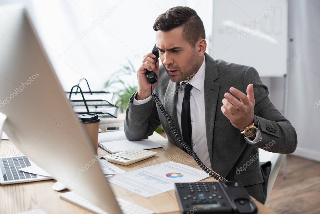 disappointed trader talking on telephone near calculator and papers with infographics, blurred foreground