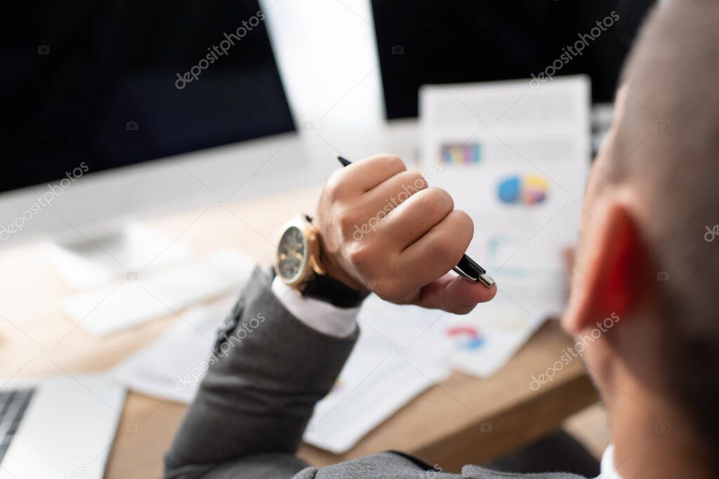 selective focus of trader holding pen while working near monitors on blurred background