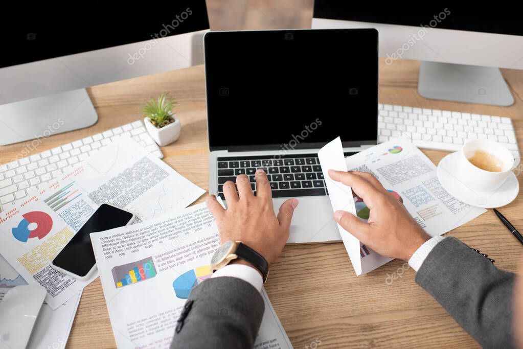 cropped view of trader typing on laptop near papers with infographics