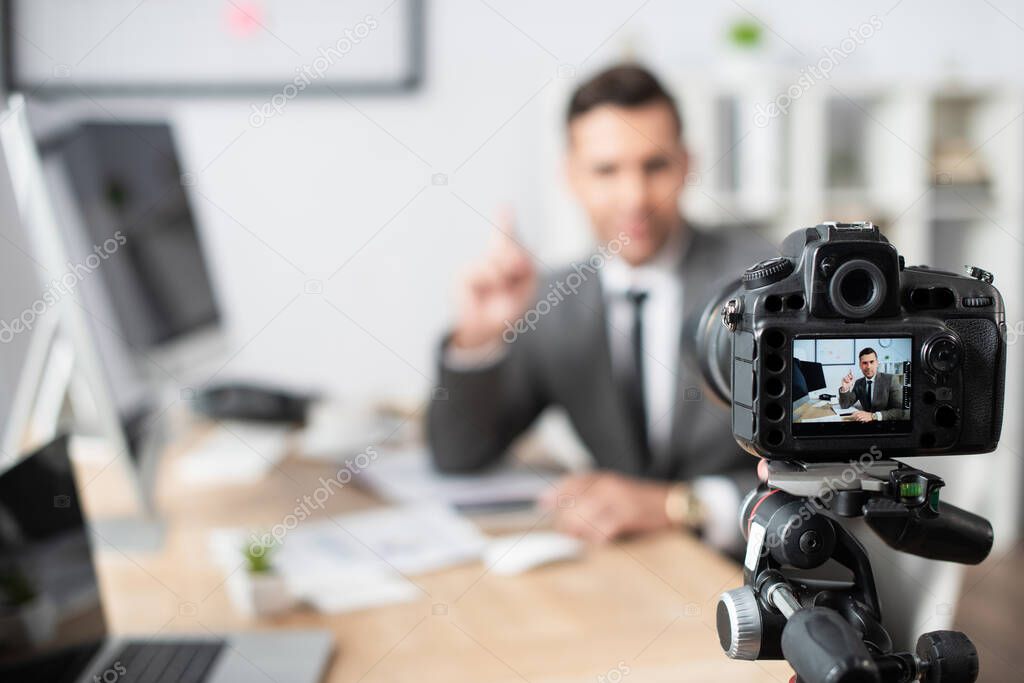 selective focus of digital camera near trader pointing with finger during online streaming on blurred background