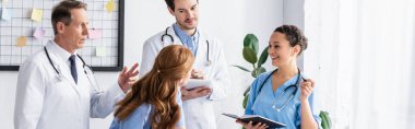 Klinikte çalışan dijital tabletli ve not defterli çok kültürlü hastane personeli. 