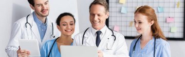 Hemşirelerle gülümseyen çok ırklı doktorlar hastanede cihaz ve afiş kullanıyorlar. 
