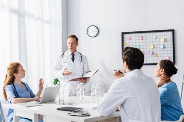 Klinikte dizüstü bilgisayar ve kağıt klasörleriyle çalışan çok ırklı hastane personeli 