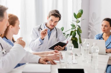 Not defterli doktor, klinikte dizüstü bilgisayarı olan Afrikalı Amerikalı hemşirelere bakıyor. 