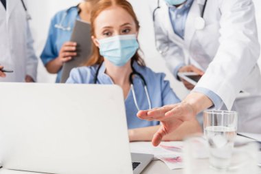 Bulanık ön planda meslektaşlarının yanındaki bilgisayarı gösteren doktor.