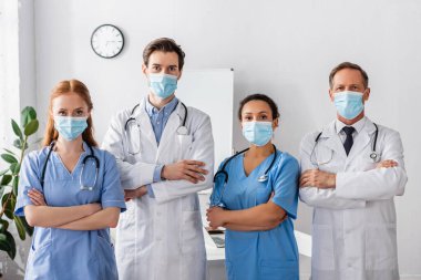 Tıp maskeli çok kültürlü doktorlar ve hemşireler hastanede yan yana dururken kameraya bakıyorlar.