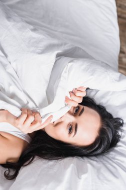 top view of young brunette woman in bed under blanket clipart