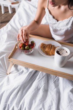 Genç esmer bir kadının kahvaltıda kakao, kruvasan ve çilek yediği görüntüler.