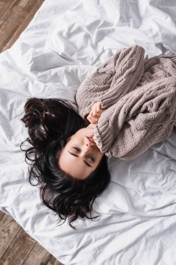 top view of young brunette woman in sweater sleeping in bed at morning clipart