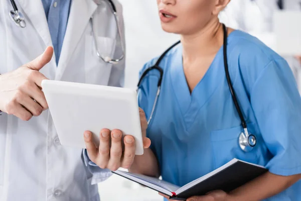 医生拿着数码平板电脑靠近护士并带着笔记本在诊所的剪影 — 图库照片