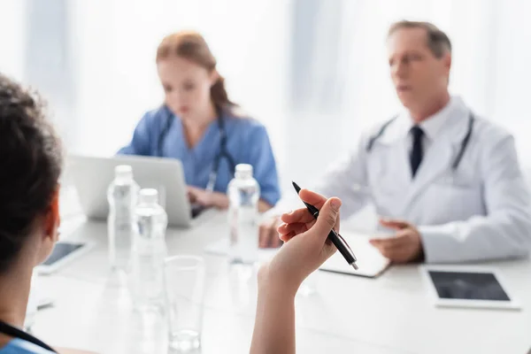 African American Nurse Holding Pen Colleagues Blurred Background Clinic — Stock Photo, Image