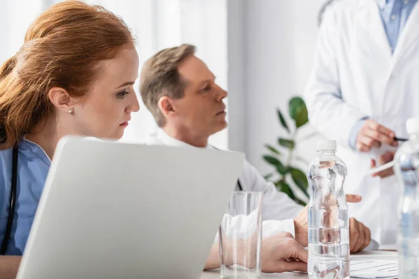 Nurse Sitting Laptop Bottles Water Colleagues Blurred Background Hospital — Stock Photo, Image