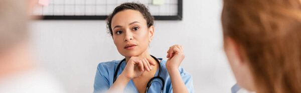 Африканская американская медсестра смотрит на коллегу на размытом переднем плане, баннер