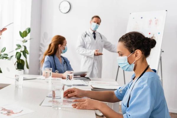 African American Nurse Medical Mask Looking Documents Water Colleagues Blurred — Stock Photo, Image