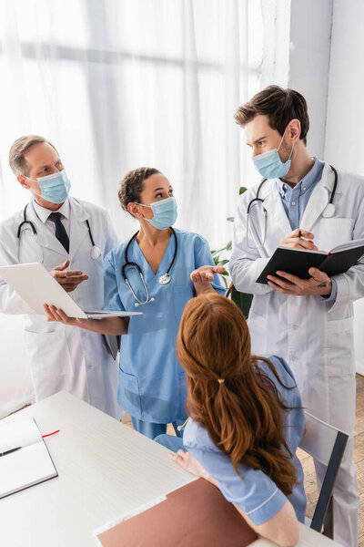 Африканская американская медсестра в медицинской маске разговаривает с врачом, стоя рядом с коллегами в больнице