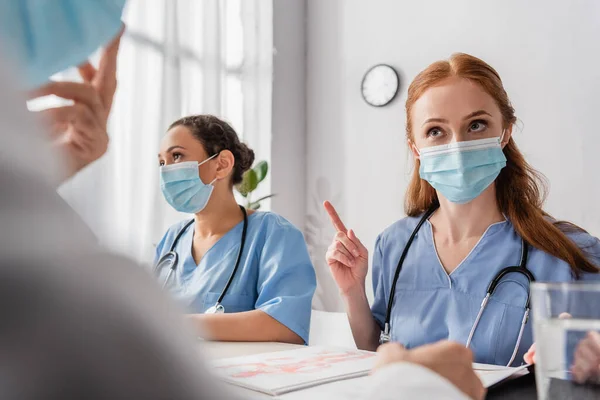 Enfermera Pelirroja Mostrando Gesto Advertencia Mientras Sienta Con Colegas Multiculturales — Foto de Stock