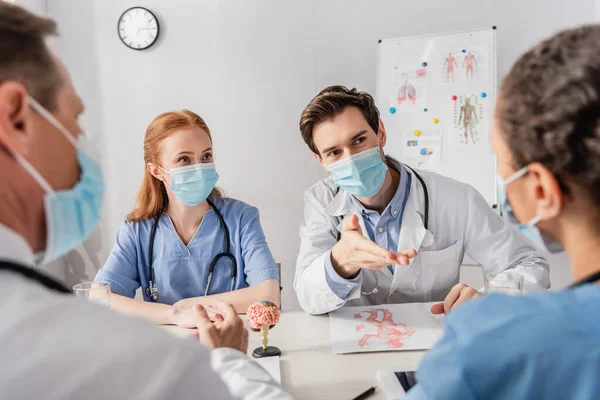 Médico Sentado Cerca Colegas Mientras Señala Con Mano Borrosa Enfermera — Foto de Stock