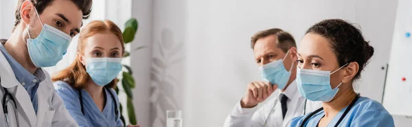 Multiethnic hospital staff in medical masks in hospital on blurred background, banner