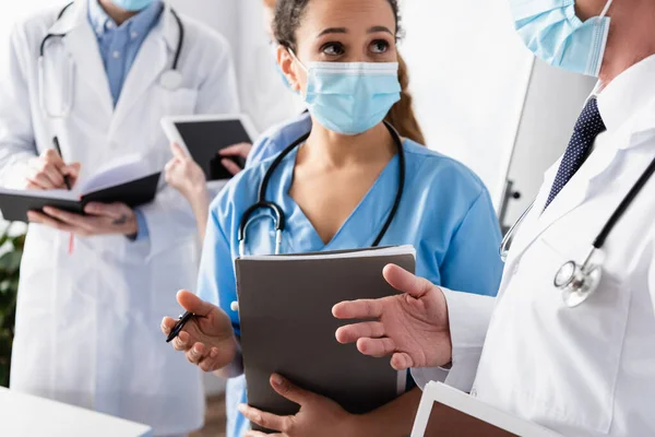 African American Nurse Medical Mask Talking Doctor Blurred Colleagues Background — Stock Photo, Image