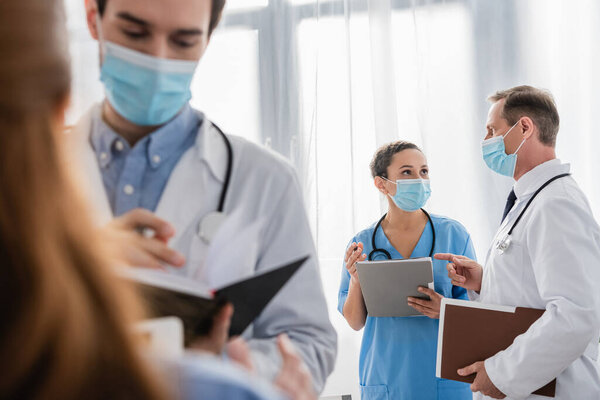 Африканская американская медсестра с бумажной папкой разговаривает с доктором с размытыми коллегами на переднем плане