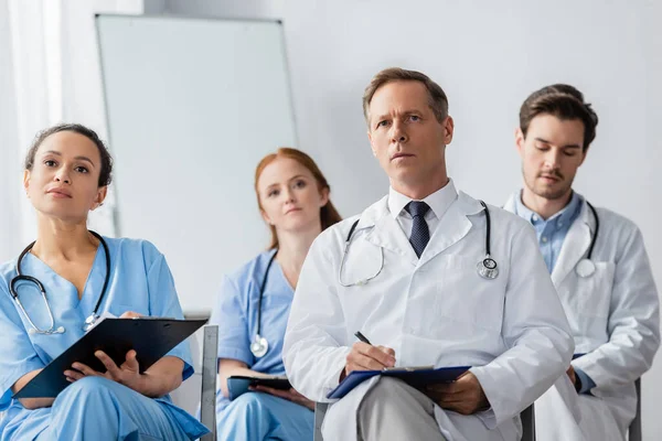 Focused Multicultural Nurses Doctors Clipboards Looking Away Meeting Hospital Blurred — Stock Photo, Image